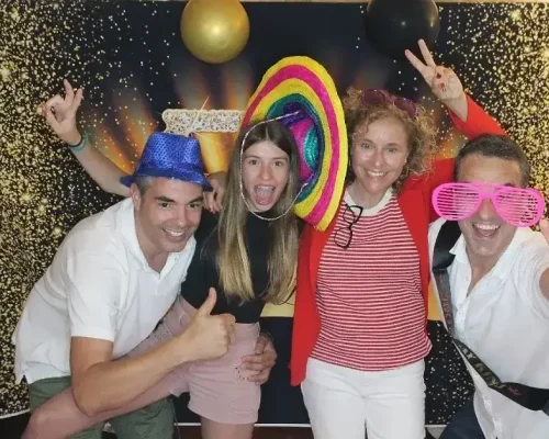 Una feliz familia posa divertida frente a un fotomaton. Usan gorros de colores y atrás hay un fondo lleno de luces | FOTOMATON COSTA BRAVA